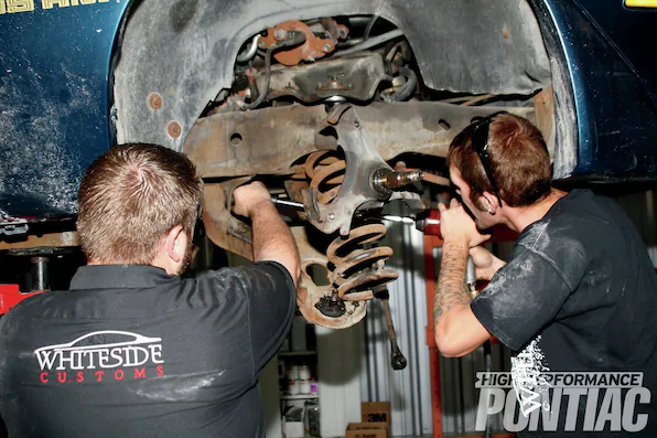 13. To provide enough clearance for the spring to be pulled out, a 21mm wrench and flex-head socket on an extension were used to loosen the bolts and twist the control arm enough for the spring to fall out.