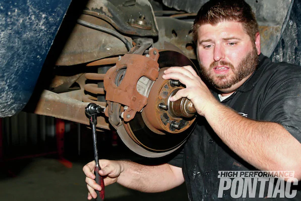 3. The first step in installing the Gen II racing suspension is to get the Firebird on a lift and remove the two front wheels to gain access to the control arms, springs, and sway bar. The calipers are then removed with a 3⁄8-inch Allen hex-head socket, and the two long bolts on top and bottom are extracted.