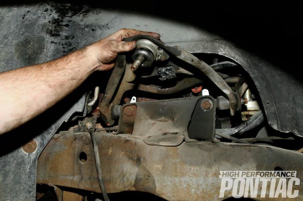 15. To finish removing the upper control arm, the spindle was removed along with the two upper-control-arm bolts. The control arm is lifted and a 13⁄16-inch socket and 3⁄4-inch wrench on the backside are used in combination to remove the remaining bolts.